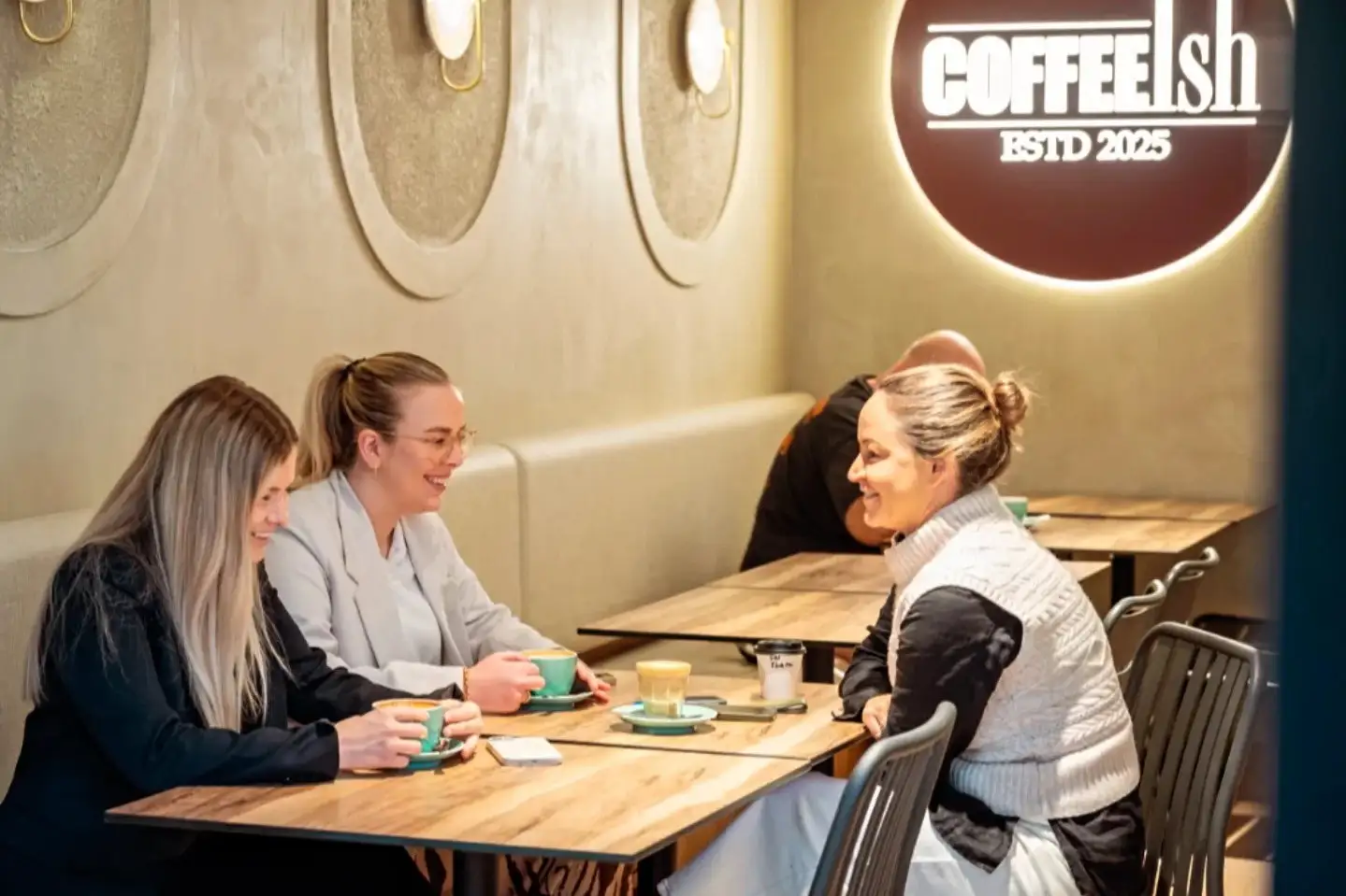 Customers at a table inside CoffeeIsh, mint cups on the table, the lit sign behind.