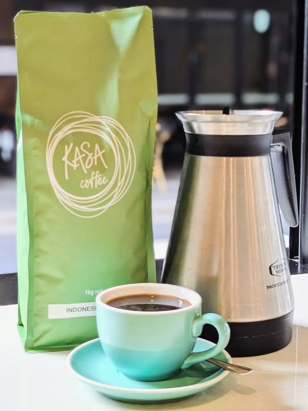 A bag of Kasa Coffee beans beside an espresso in a mint cup.