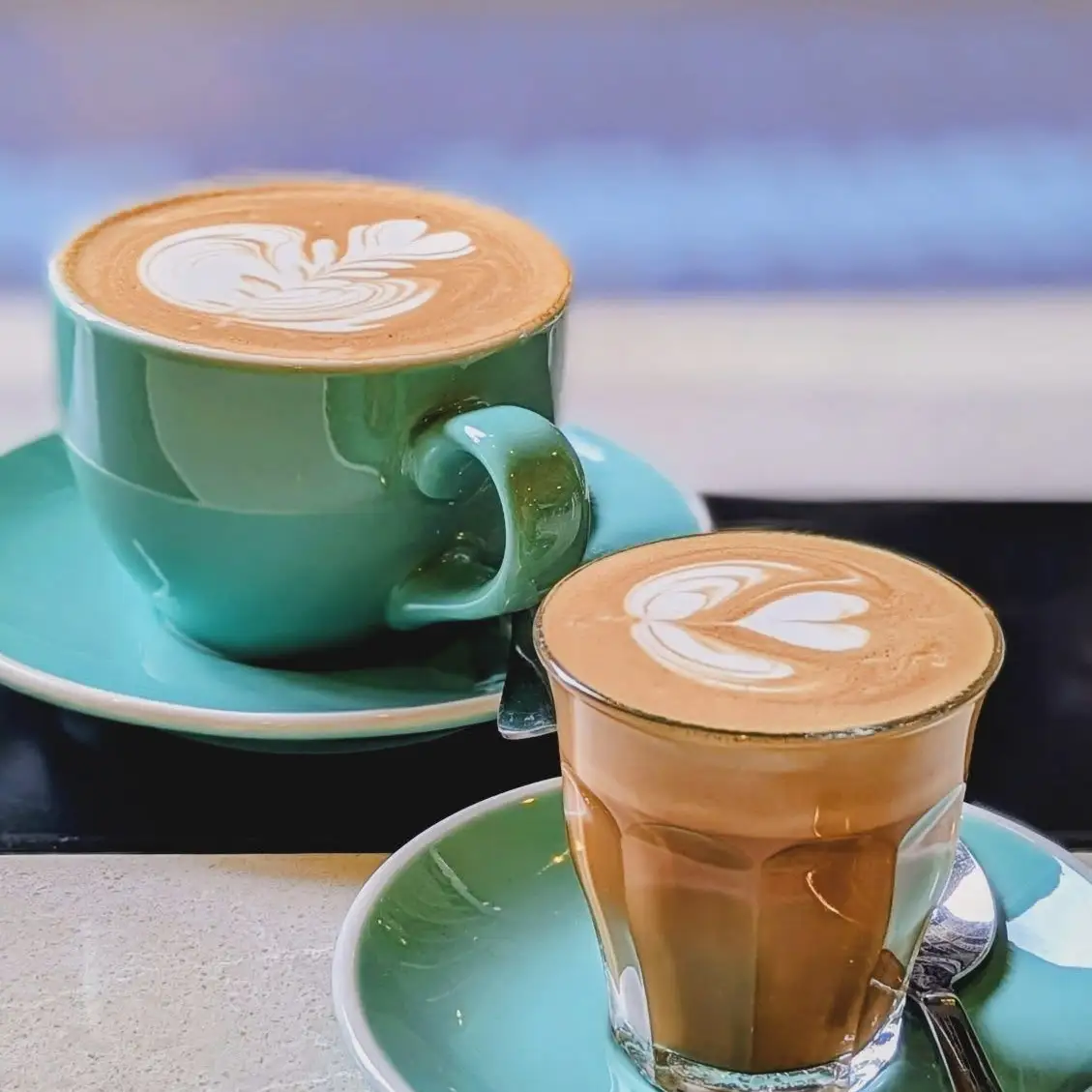 A cappuccino and a piccolo in mint green cups.