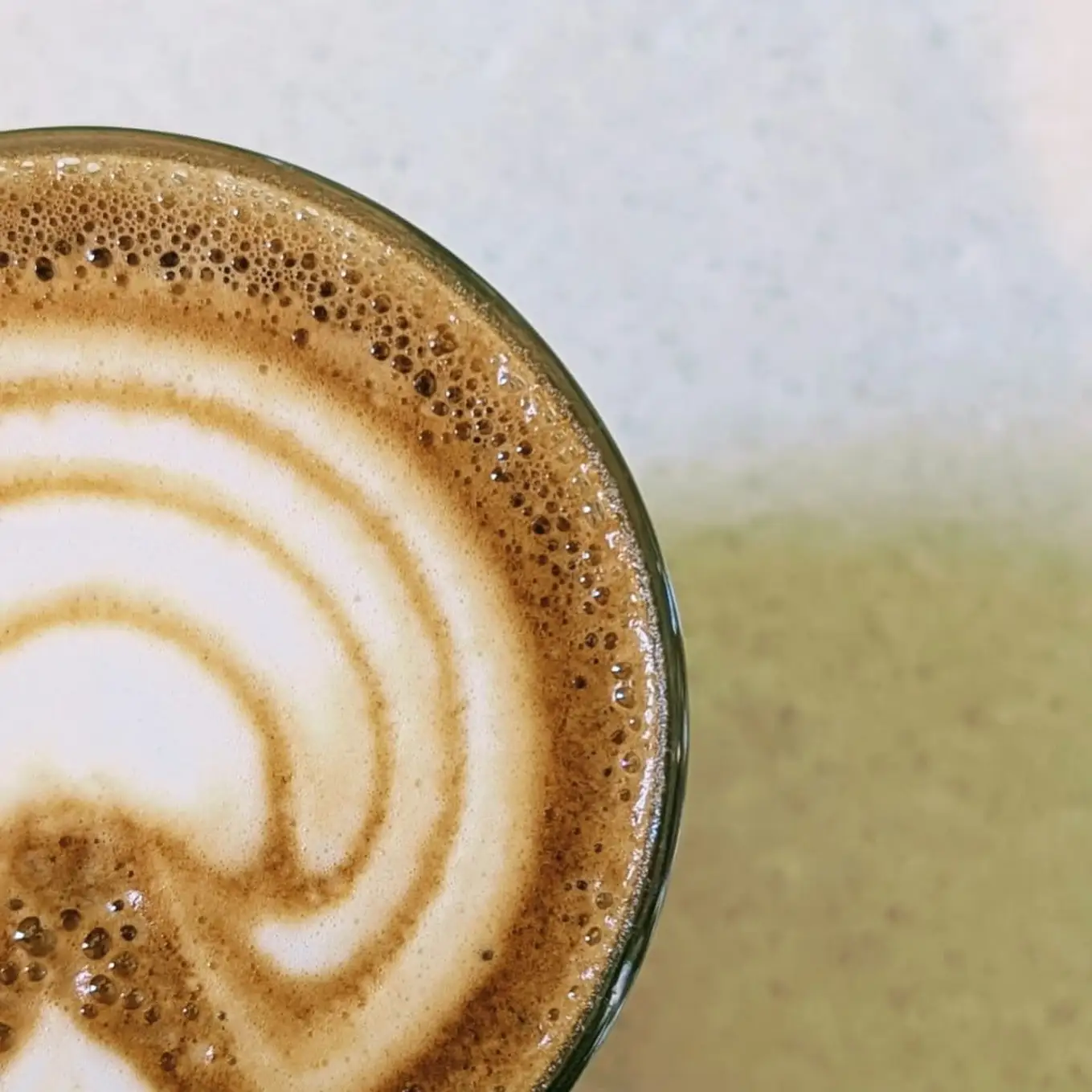 Latte art close up, a rosetta in a mint green cup.