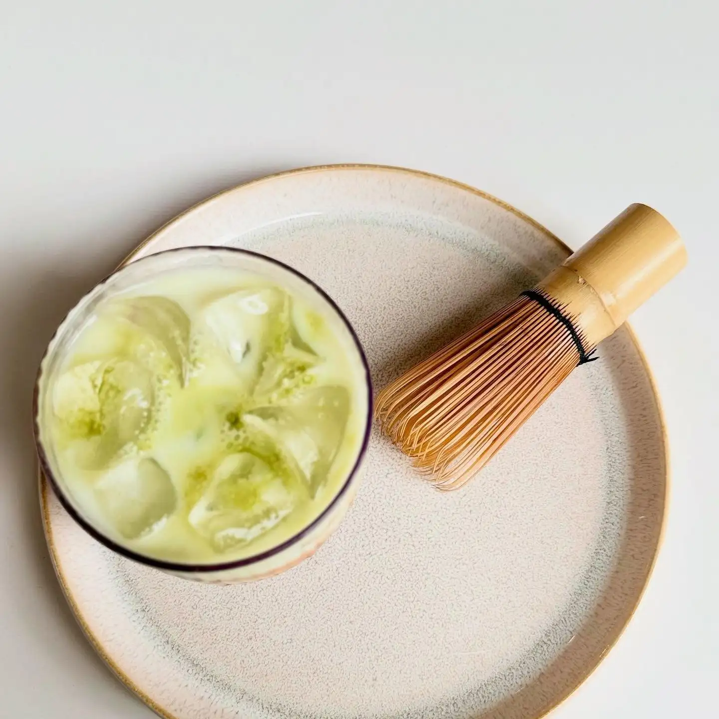 An iced matcha seen from above with a bamboo whisk.