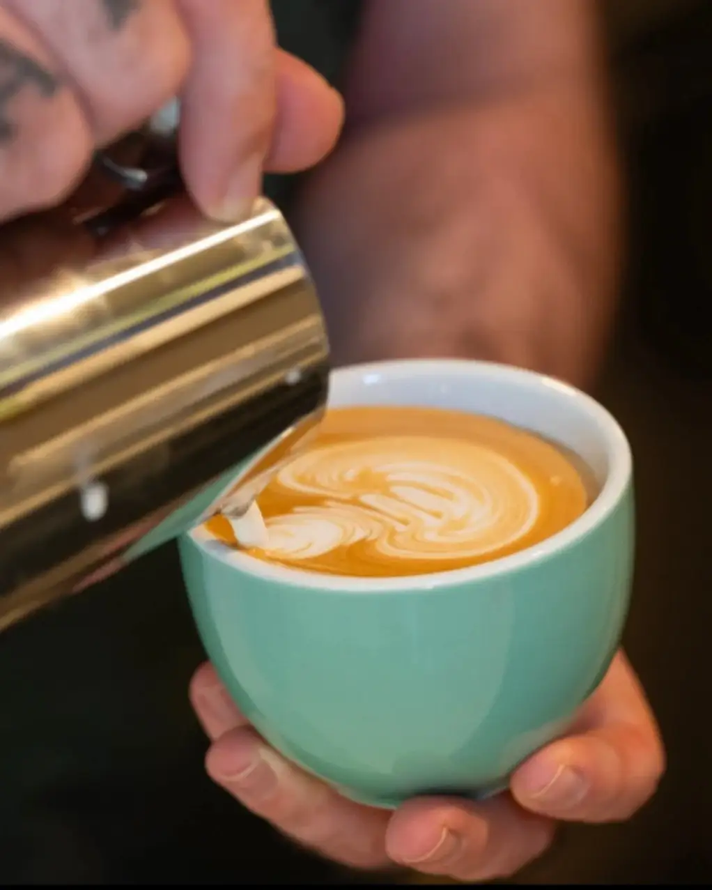 Milk being poured into a mint green cup, the latte art forming.